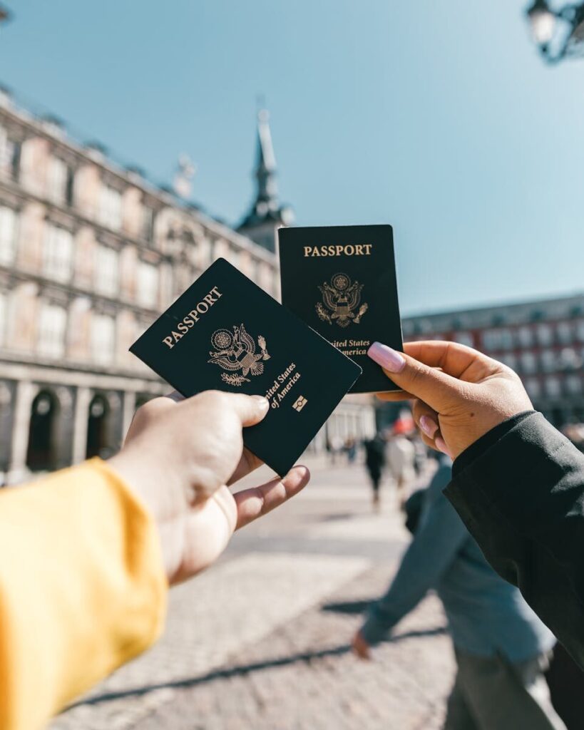 Crop unrecognizable travelers in casual clothes demonstrating passports of United States of America standing on square in historical city district